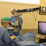 Se ve al cirujano trabajando en el microscopio, junto a él su instrumentista